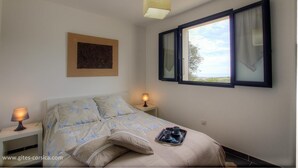 A bedroom with a bed, two bedside lamps, a window with curtains, a painting on the wall, and a tray with cups on the bed. - Apartment in the maquis facing the sea, 5mm from the beach and shops (Cargèse)