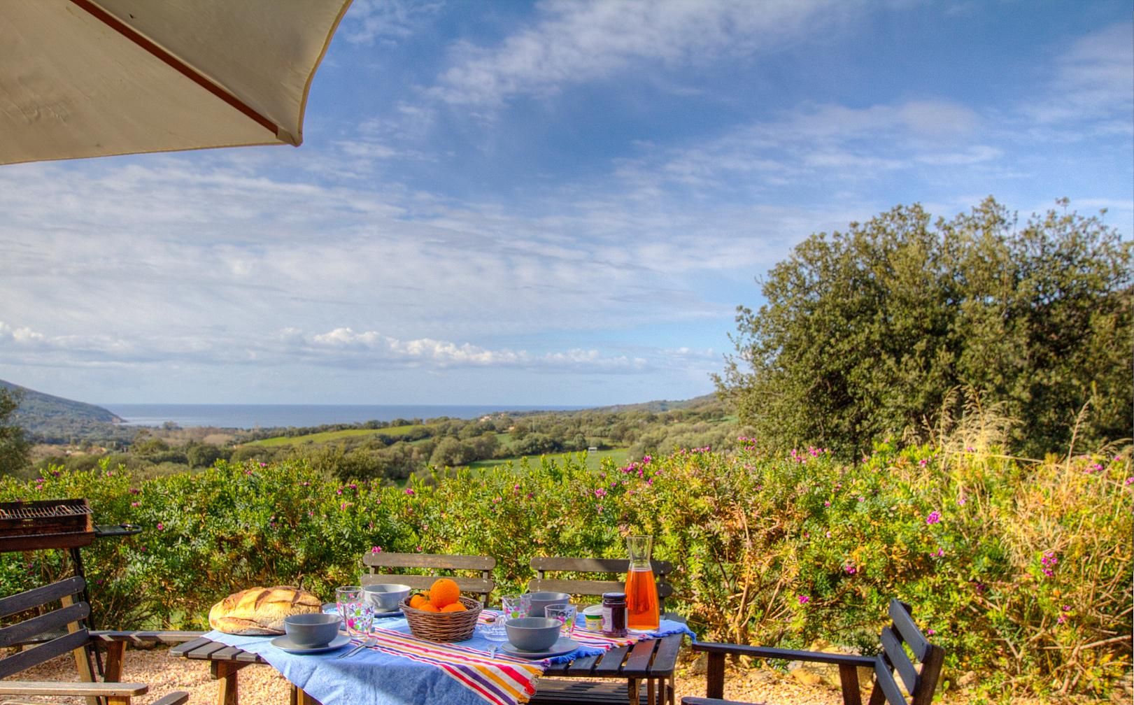 An outdoor dining setup with a table set for two, overlooking a vineyard and distant hills.