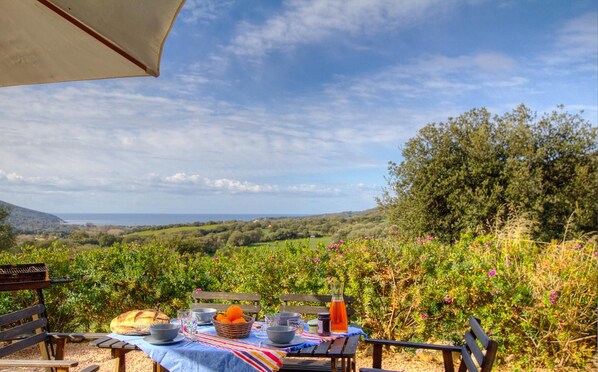An outdoor dining setup with a table set for two, overlooking a vineyard and distant hills.