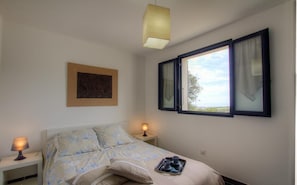 A bedroom with a bed, two bedside lamps, a window with curtains, a painting on the wall, and a tray with cups on the bed.
