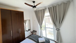 Ein Schlafzimmer mit Bett, Deckenventilator, Kleiderschrank und einem Fenster mit Vorhängen.