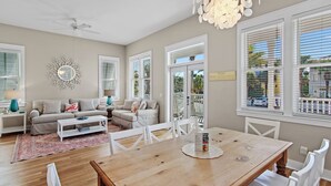 Ein geräumiges Wohnzimmer mit einem Holzesstisch, weißen Stühlen, einem grauen Sofa und einem Deckenventilator.