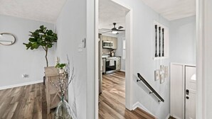 A hallway with a wooden floor, a plant, a mirror, and a door leading to a kitchen. - Casa Azul: Tranquility + Fire Pit + Gameroom + Peace (Fayetteville)