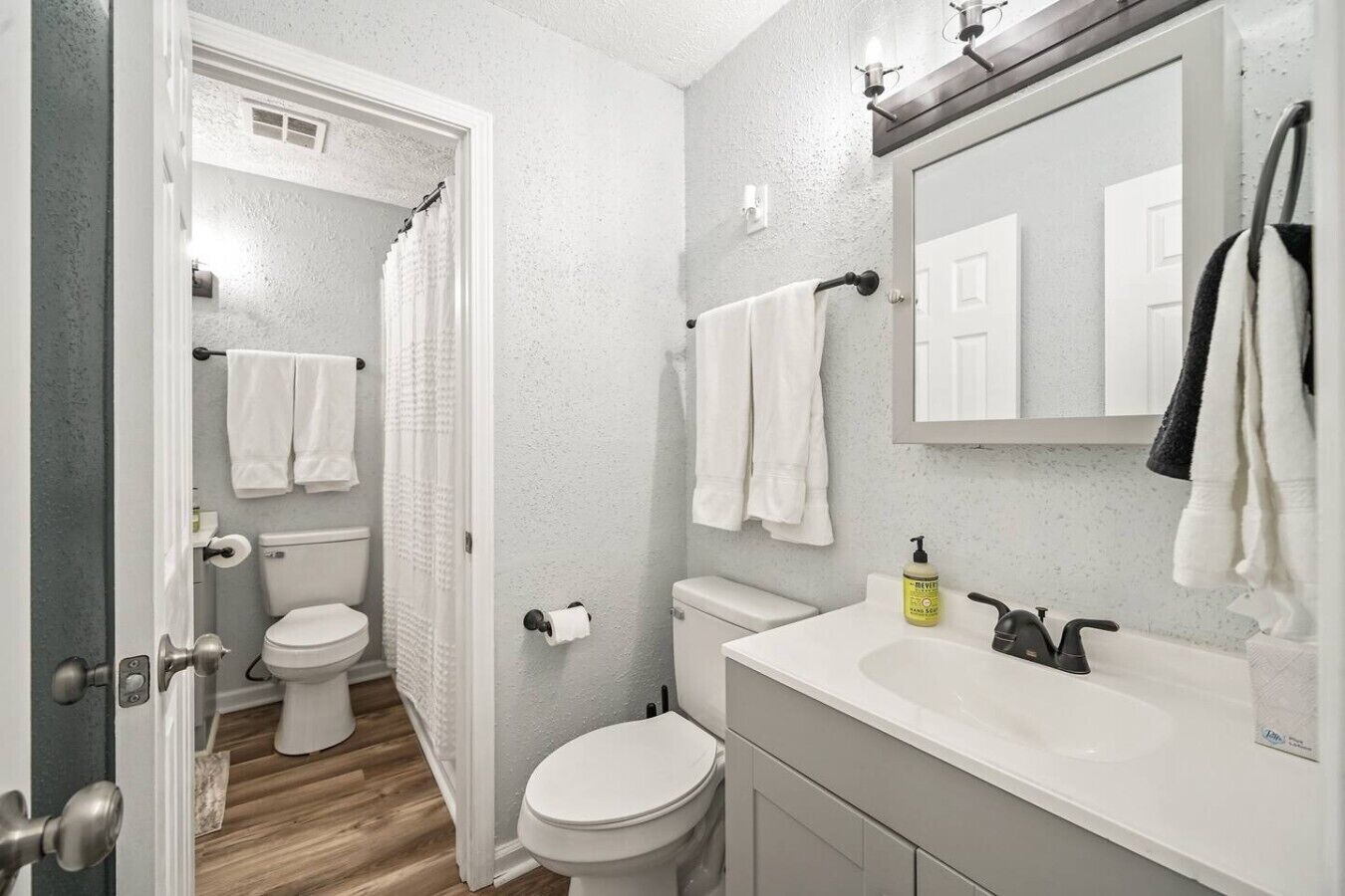 A bathroom with a toilet, shower, sink, and a mirror.
