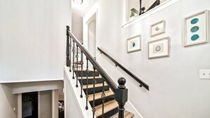 A staircase with wooden steps and black balusters, white walls, and framed artwork. - Casa Azul: Tranquility + Fire Pit + Gameroom + Peace (Fayetteville)