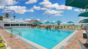 Ein Swimmingpool mit klarem, blauem Wasser, umgeben von Liegestühlen und Sonnenschirmen, mit Blick auf den Ozean und einer Flagge im Hintergrund.