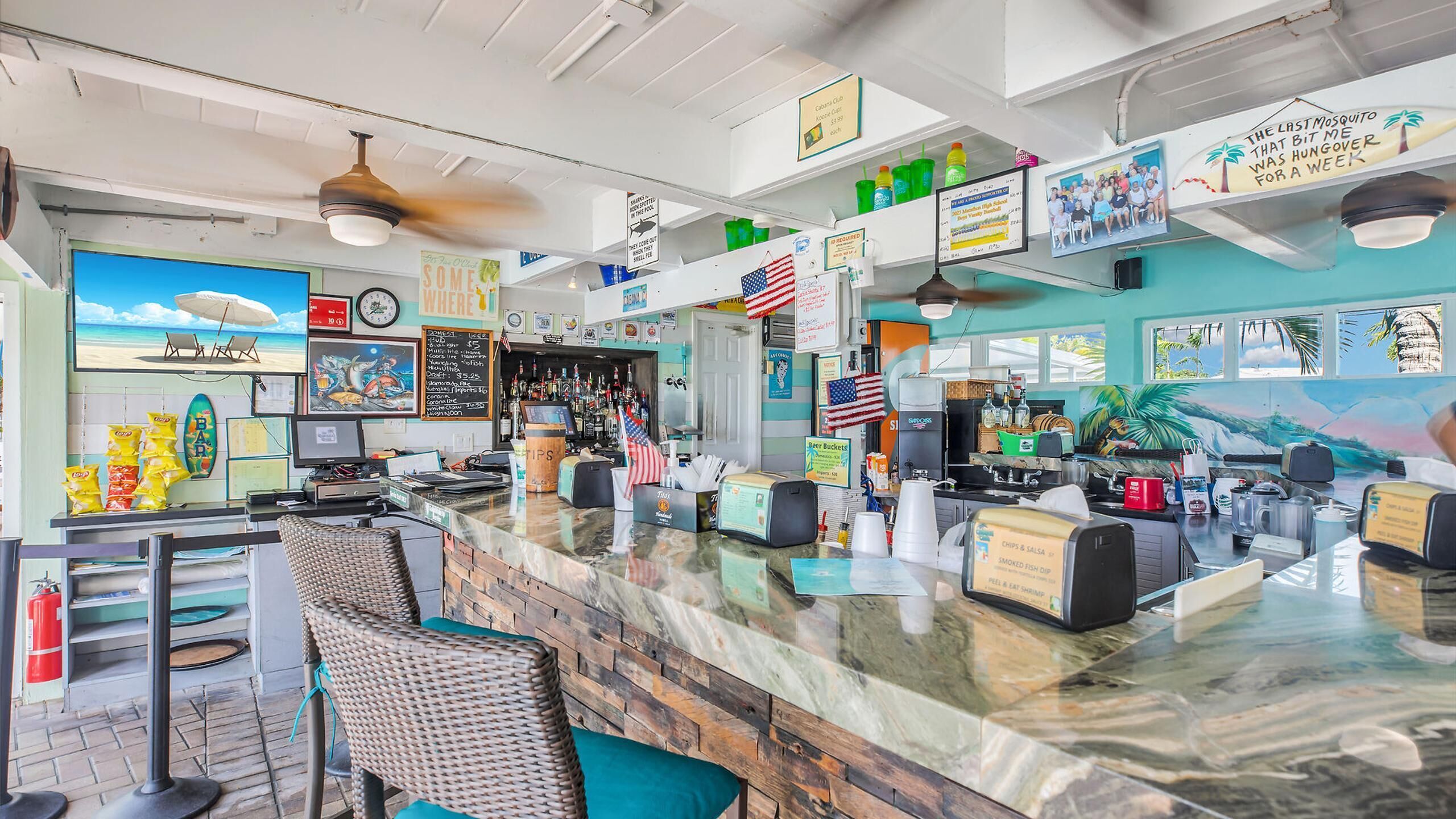 A bar with a counter, seating area, and various amenities including flags, a menu board, and a television screen.