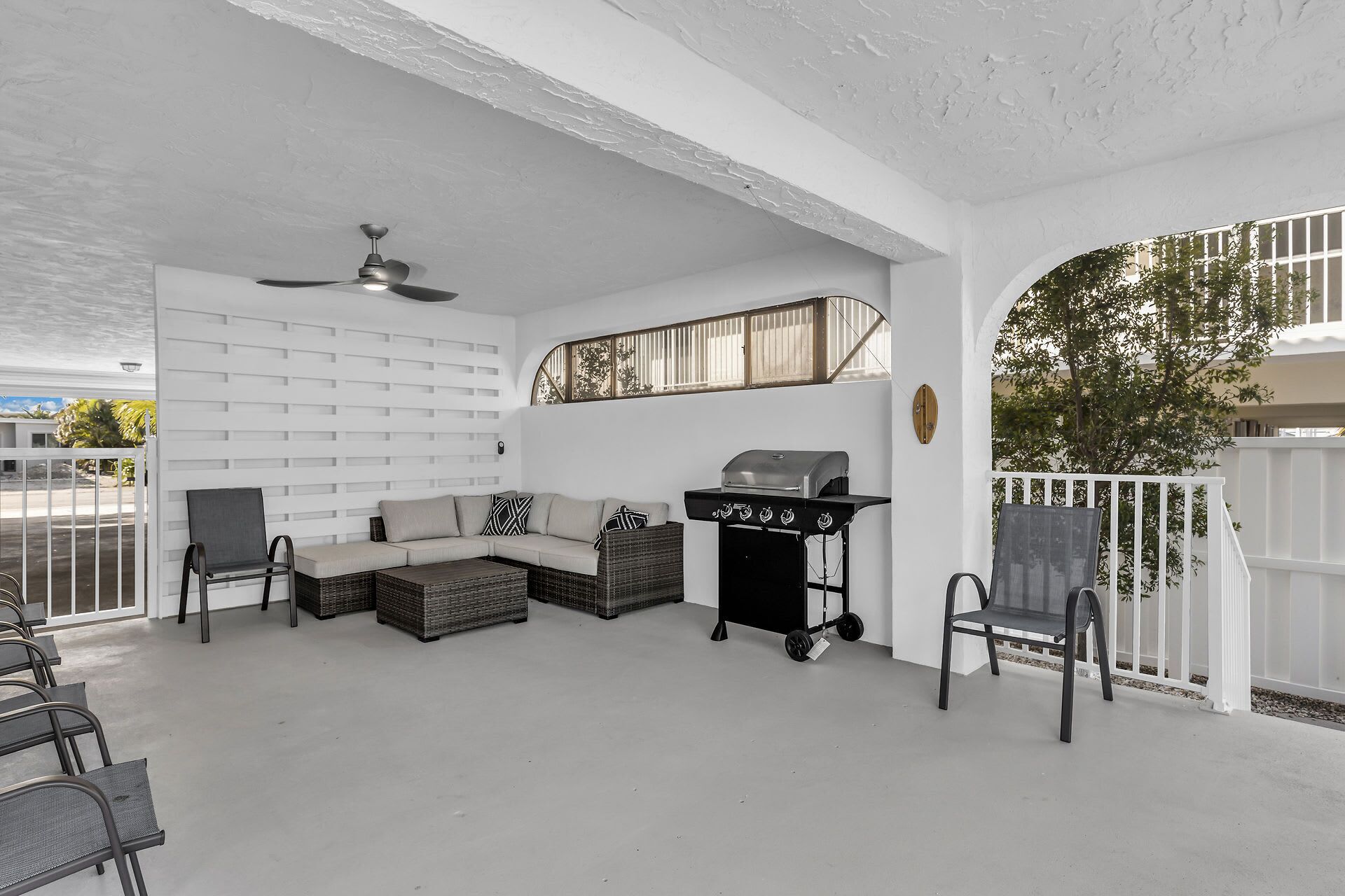 A covered patio with a ceiling fan, a sofa set, a grill, and outdoor chairs.