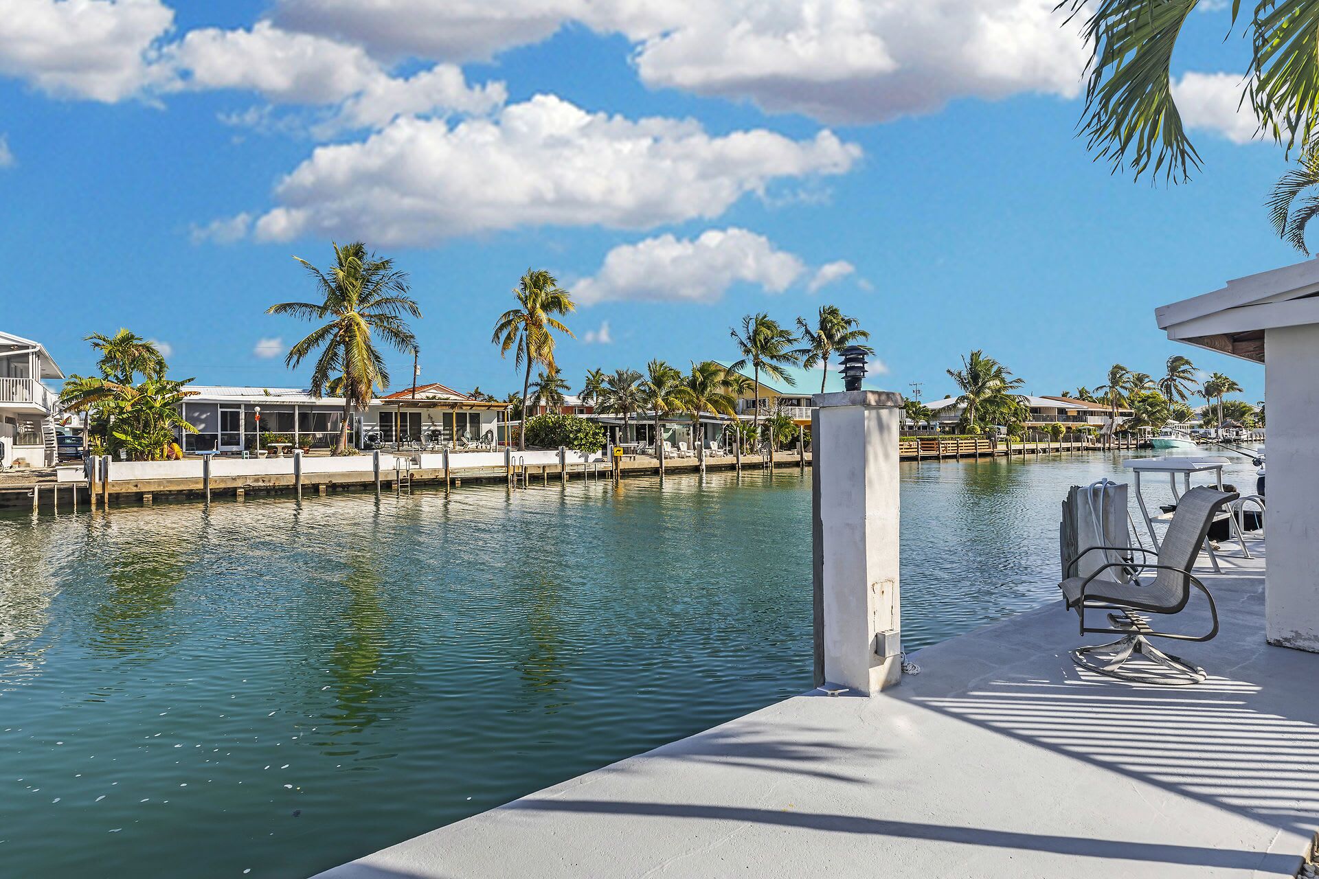A waterfront property with a pool, lounge chairs, and palm trees.
