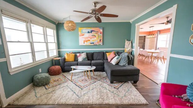 Een woonkamer met turquoise wanden, een donkere bank, een rode fauteuil en een plafondventilator.