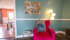 Een kamer met blauwgroene wanden, een rode fauteuil met blauw kussen, een rond bijzettafeltje en een vloerlamp met drie lampen.