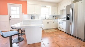 Een moderne keuken met witte kastjes, een roestvrijstalen koelkast en een zwarte barkruk.