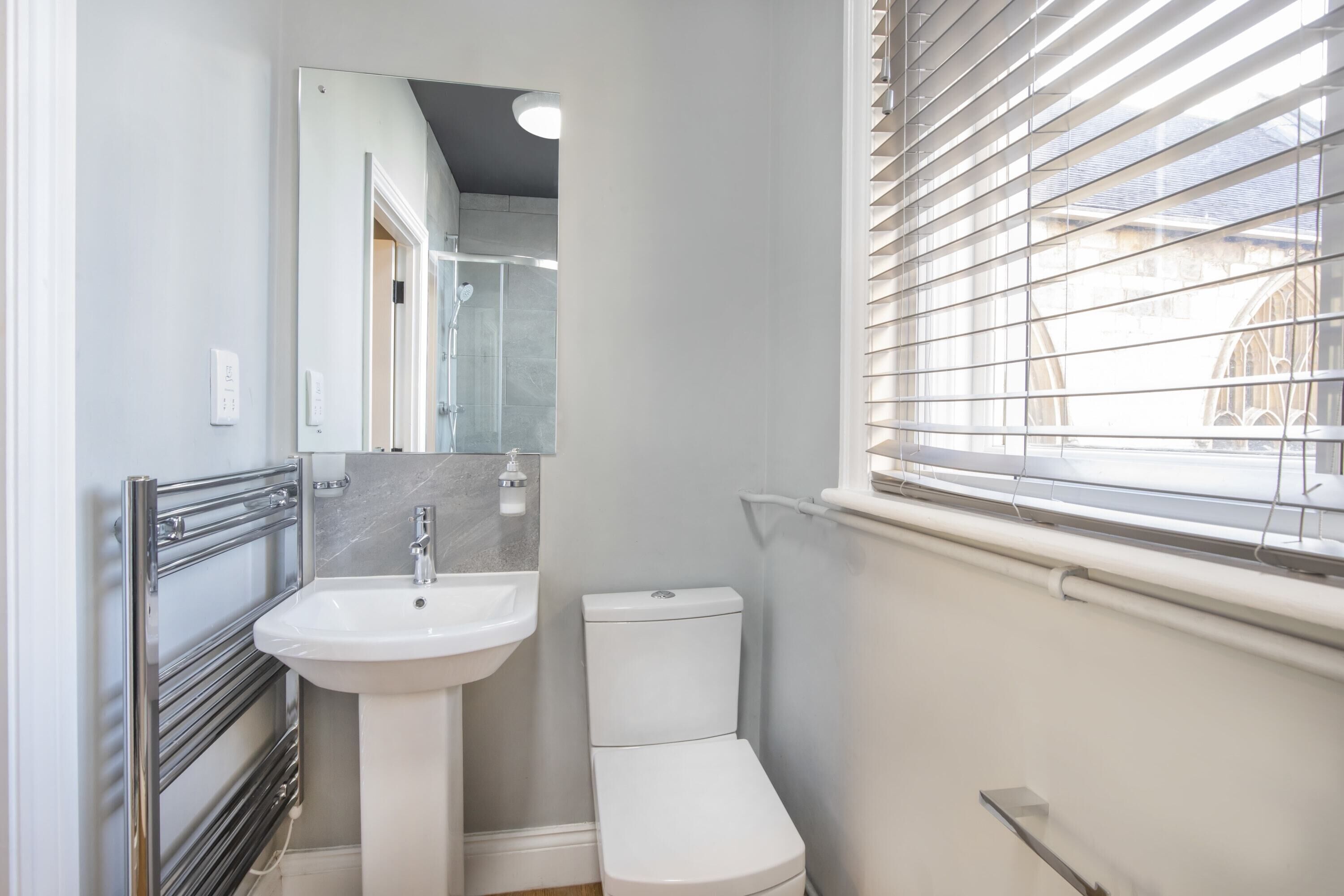 A compact bathroom with a white sink, toilet, and a window with blinds.