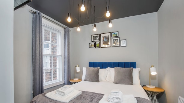 A neatly made bed with a blue headboard, two bedside tables with lamps, and a window with curtains.
