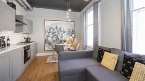 A modern kitchen with grey cabinets, a dining area with a table and chairs, and a grey sofa with patterned cushions.
