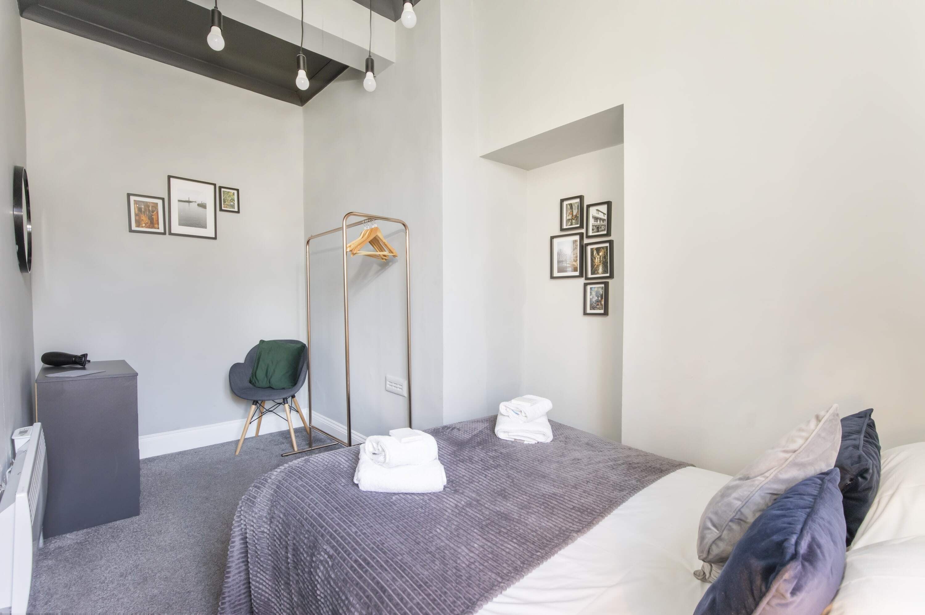 Ein modernes Hotelzimmer mit einem Bett, einem Sessel, einer Heizung, einem Kleiderhaken und gerahmten Bildern an den Wänden.