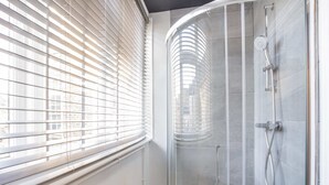 A shower with a glass door, a showerhead, and a handheld shower attachment.