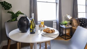 A dining area with a round table, chairs, a vase, a bottle, a glass, and a plate with croissants.