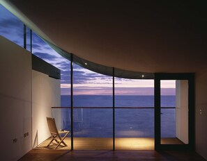 Une pièce dotée d’une grande fenêtre donnant sur la mer, d’un plancher en bois et d’une seule chaise.
