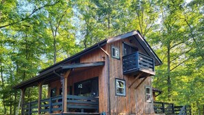 A rustic cabin with a wooden exterior, a balcony, and a stone foundation. -  Secluded ridge 
 top wilderness retreat with fast wifi and all the comforts  (Wytheville)