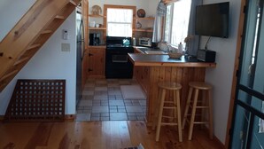 A kitchen with wooden cabinets, a black stove, a window, and a TV mounted on the wall. -  Secluded ridge 
 top wilderness retreat with fast wifi and all the comforts  (Wytheville)