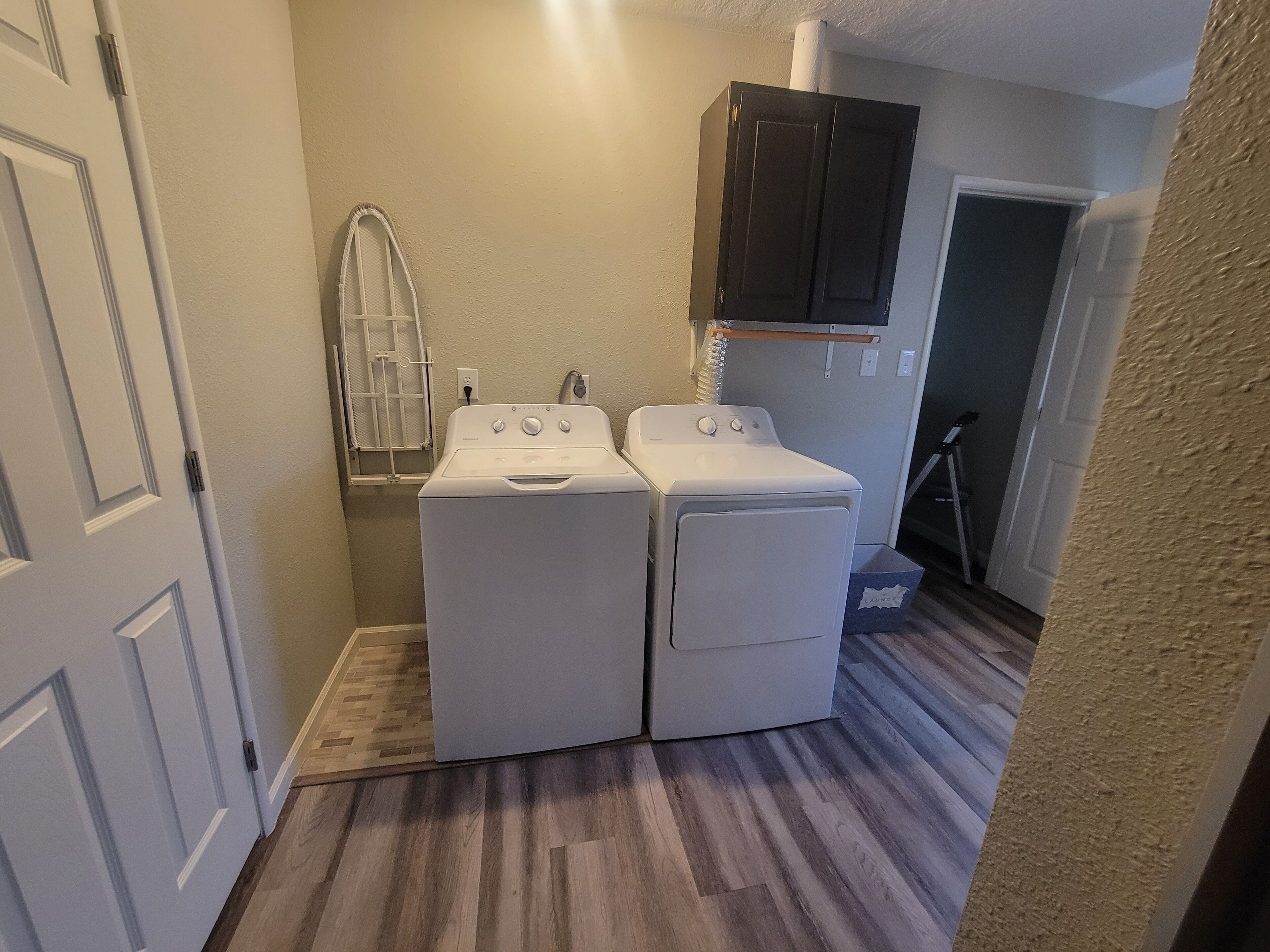 A laundry room with two white front-loading washing machines, a dryer, and a dark wooden cabinet above the dryer.