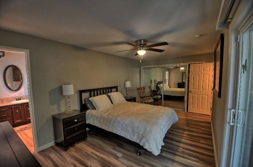 A bedroom with a bed, nightstands, a ceiling fan, a mirror, and a door leading to another room.