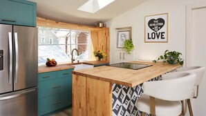 Een moderne keuken met blauwgroene kastjes, een roestvrijstalen koelkast, een houten eiland en een stoel met een zwart-wit patroon.