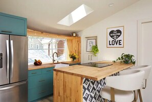 Een moderne keuken met blauwgroene kastjes, een roestvrijstalen koelkast, een houten eiland en een stoel met een zwart-wit patroon.