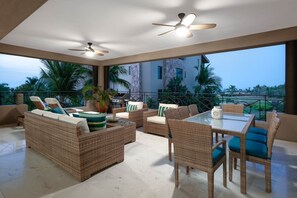 Eine großzügige Terrasse im Freien mit Korbmöbeln, Deckenventilatoren und Blick auf den Ozean.
