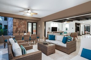 A spacious living area with wicker furniture, a ceiling fan, and a view through an open door.