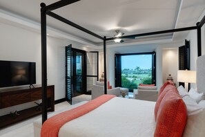Ein modernes Schlafzimmer mit Himmelbett, Fernseher, Schreibtisch und Blick auf eine grüne Landschaft.