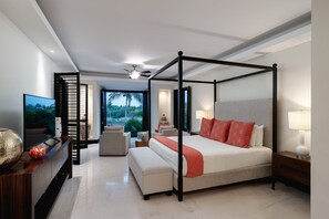 Un lit Ă baldaquin donnant sur un paysage verdoyant, un tĂ©lĂ©viseur Ă Ă©cran plat, un coin salon avec un canapĂ© et des fauteuils, et une table dâappoint en bois avec une lampe.