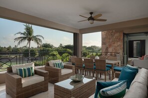 Ein Balkon mit Korbmöbeln, einem Deckenventilator und Blick auf Palmen.