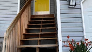 A wooden staircase leading to a yellow door, a green potted plant, and a wall-mounted light fixture. - Newly Remodeled 3 Bed 2 Bath home, minutes from everything (Pendleton)