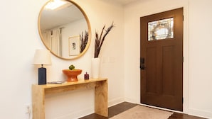 A hallway with a wooden console table, a round mirror, a vase with dried plants, and a brown door with a window. - Luxurious 5-Bedroom Lakeside Retreat with Hot Tub, Fire Pit and Dolly Room (Hendersonville)
