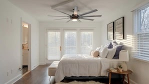 A bedroom with a bed, a ceiling fan, a window with blinds, and a small bedside table with a lamp. - Luxurious 5-Bedroom Lakeside Retreat with Hot Tub, Fire Pit and Dolly Room (Hendersonville)