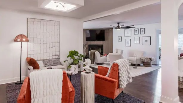 A modern living room with a fireplace, a ceiling fan, and a large abstract painting on the wall. - Luxurious 5-Bedroom Lakeside Retreat with Hot Tub, Fire Pit and Dolly Room (Hendersonville)