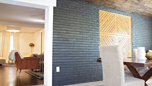 A modern living room with a dark brick wall, a wooden panel design, a dining area with a table and chairs, and a cozy seating area with a chair and a lamp. - Luxurious 5-Bedroom Lakeside Retreat with Hot Tub, Fire Pit and Dolly Room (Hendersonville)