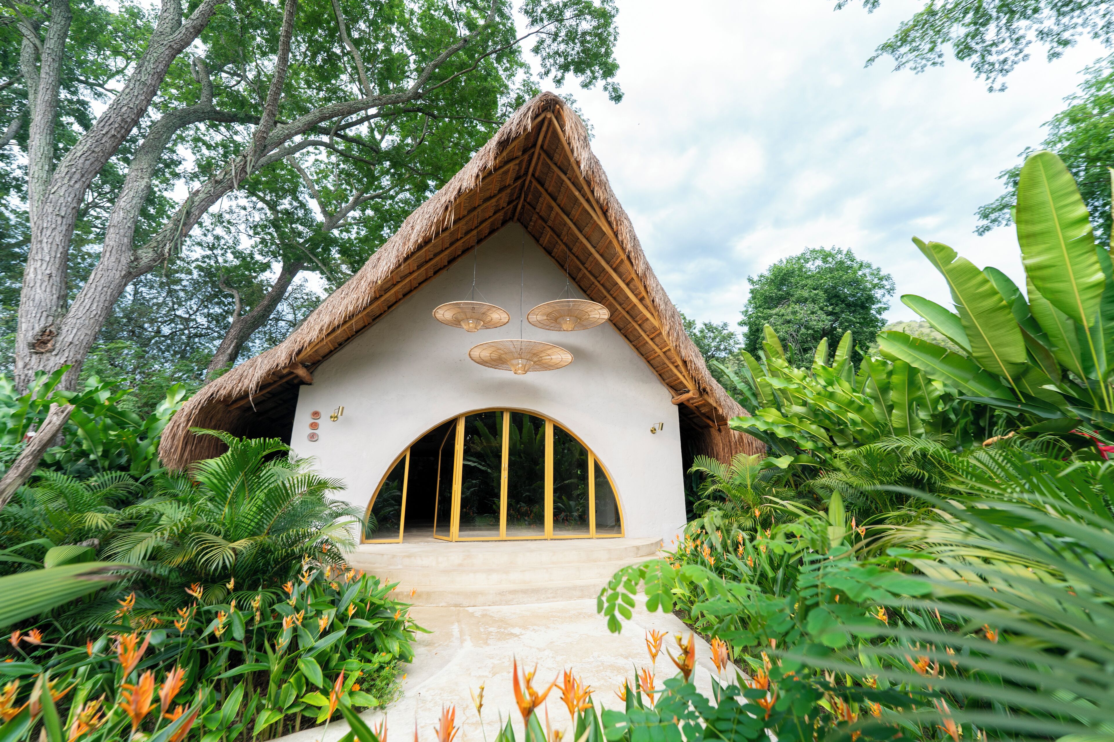 A thatched-roof hut with a large arched entrance, surrounded by lush tropical vegetation.