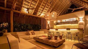 A cozy lounge area with a thatched ceiling, a bar with a 'BAR' sign, and a seating arrangement including a sofa and chairs. - Nativa Refugio Escondido (Sopetrán)