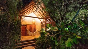 A cozy, thatched-roof structure surrounded by lush greenery, with a hammock and a wooden door leading inside. - Nativa Refugio Escondido (Sopetrán)