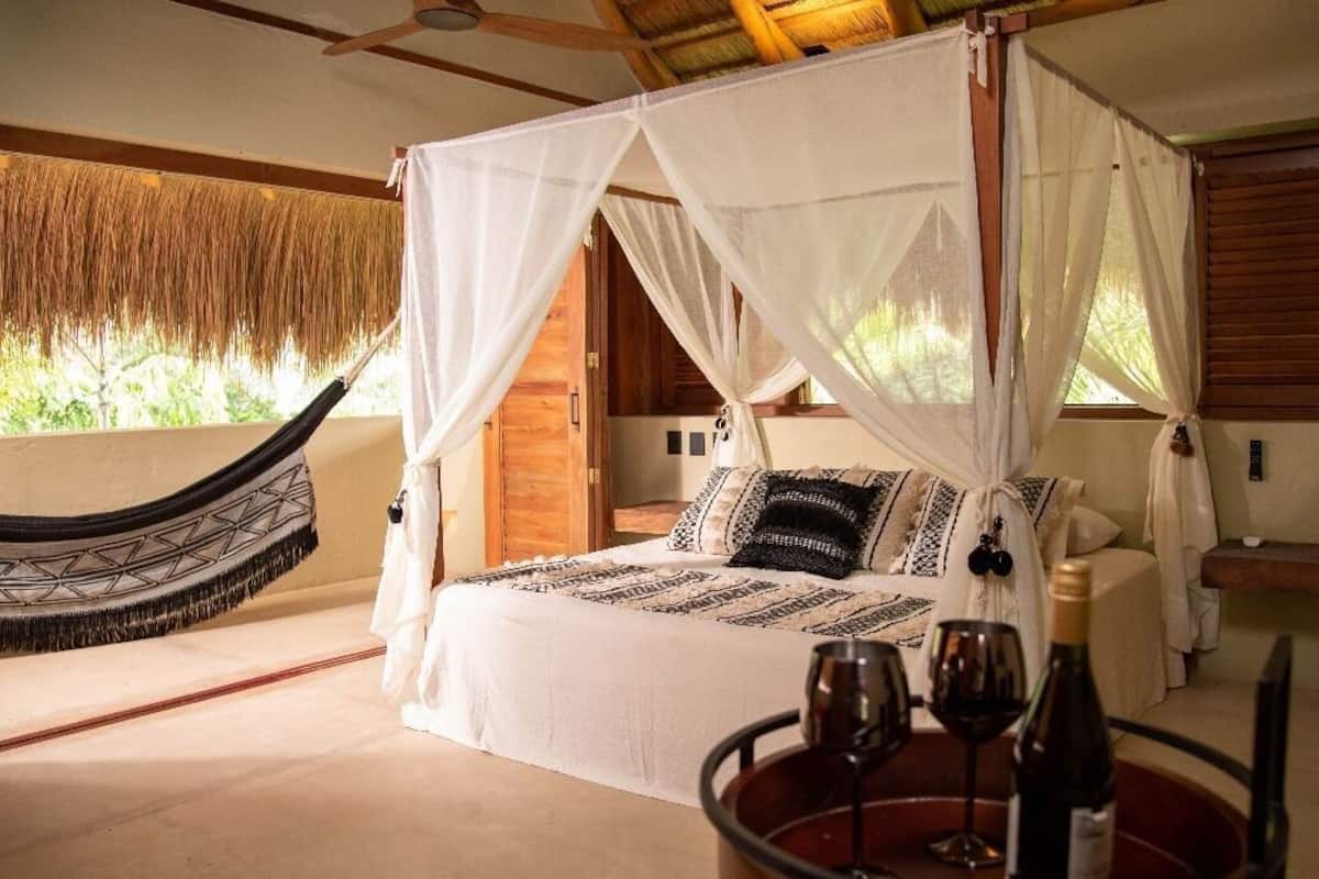 A four-poster bed with a canopy, a hammock, and a dining table with wine glasses.