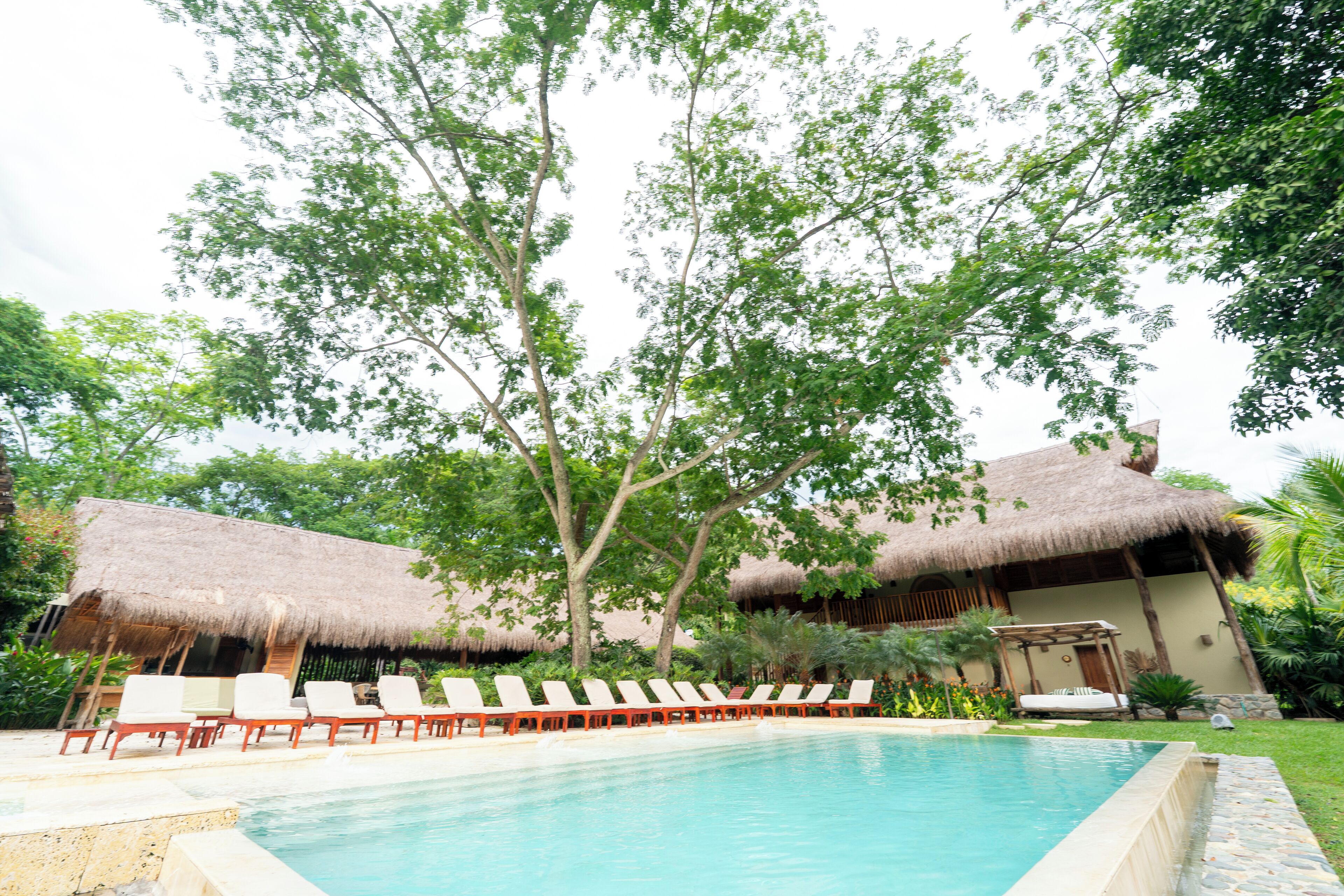 A pool area with lounge chairs and thatched-roof structures.