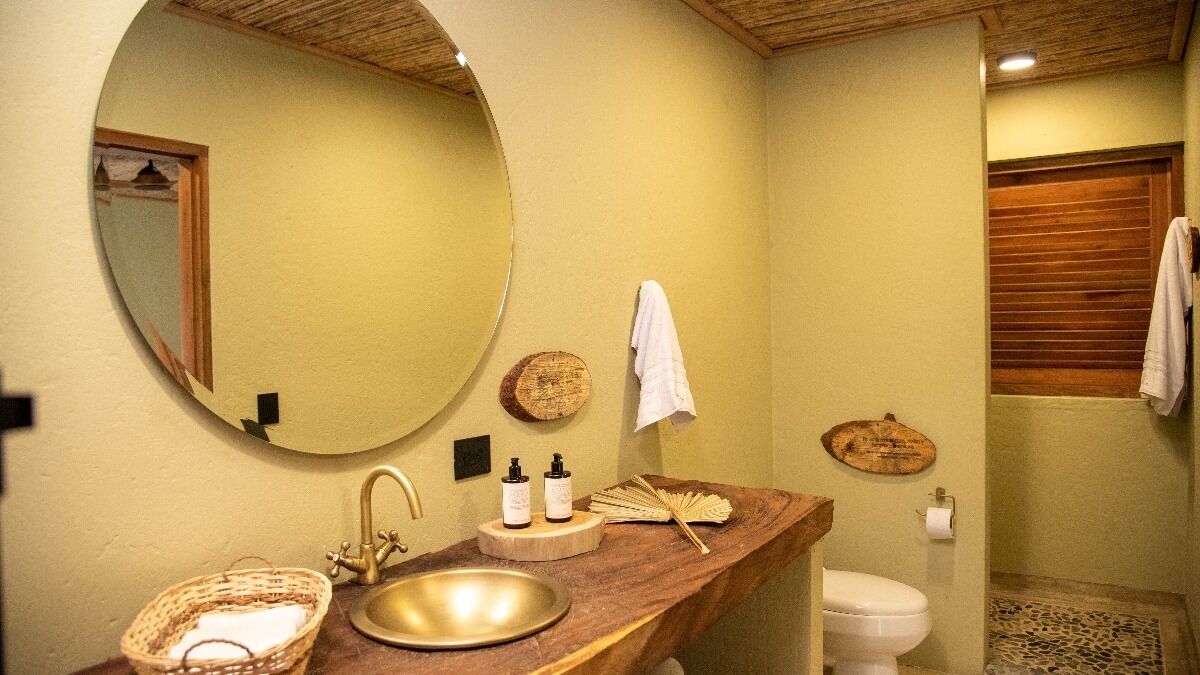 Een badkamer met een ronde spiegel, houten wastafelmeubel, wastafel en toilet.