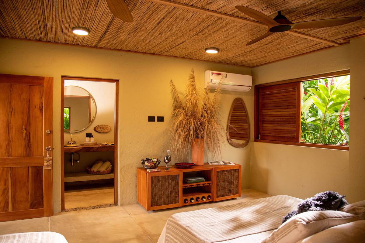 A bedroom with a wooden ceiling, a bed, a wooden cabinet, and a window with a view of greenery.