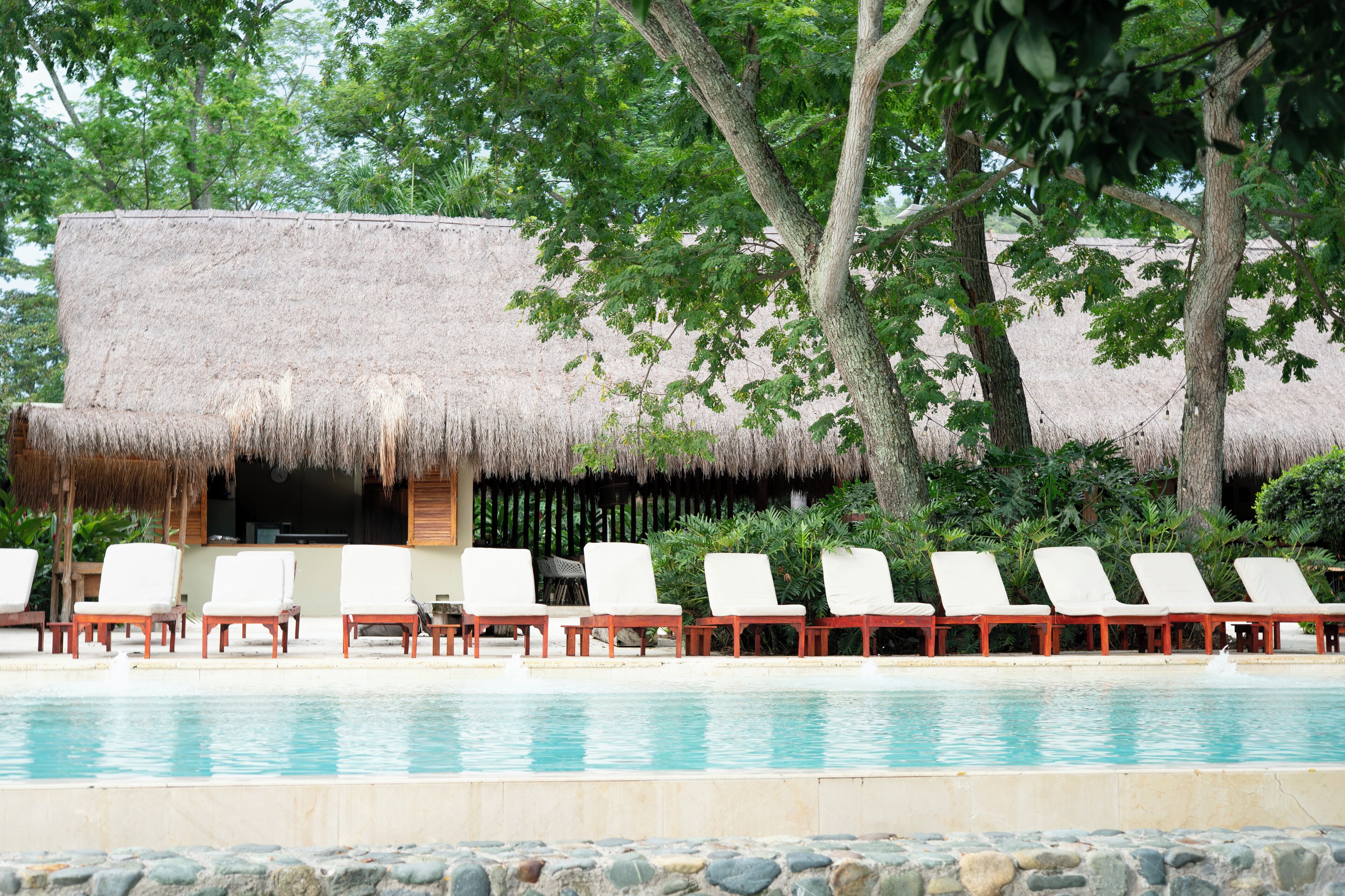 A pool area with lounge chairs and a thatched-roof structure.