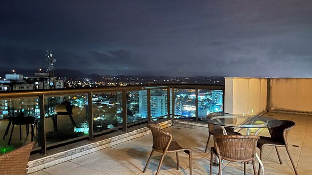 Une terrasse sur le toit, dotée d'une balustrade en verre, de mobilier en osier et offrant une vue sur la ville la nuit.