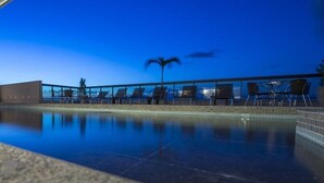 Un espace aménagé au bord de la piscine, avec des chaises longues et un palmier, dont le reflet se mire dans l’eau.
