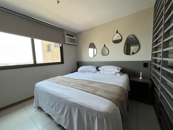 Une chambre d’hôtel avec un grand lit, une fenêtre, un appareil de climatisation et un miroir fixé au mur.